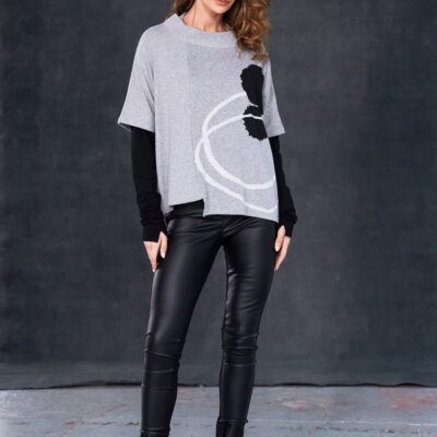 Model wearing black NAYA leatherette leggings paired with a grey abstract-print layered top, standing against a dark studio background.