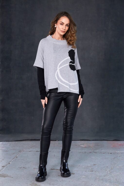 Model wearing black NAYA leatherette leggings paired with a grey abstract-print layered top, standing against a dark studio background.