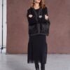Model wearing NAYA round neck dress with mesh skirt and frill hem (NAW25277), layered with a black textured jacket and paired with patent ankle boots, standing against a brown backdrop.