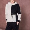 Model wearing NAYA two tone funnel neck top in sand and black with abstract print (NAW25262), paired with black trousers, posing against a muted pink backdrop.